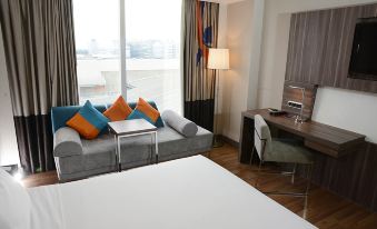 a modern hotel room with a couch , bed , and desk , along with a window offering a view of the city at Novotel Bangkok Impact