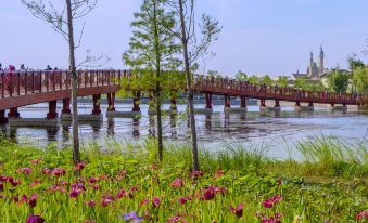 There is a bridge over the water adorned with red flowers, flanked by trees on both sides at Shanghai Disneyland Hotel