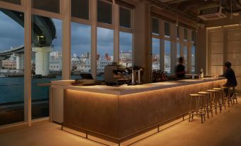 a modern coffee shop with a large window offering a view of the city , and several people sitting at the counter at Hotel Anteroom Naha