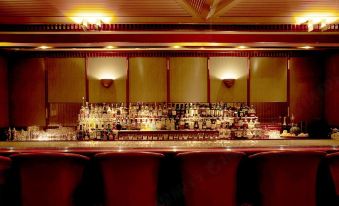 a long bar with multiple bottles and glasses , along with two red chairs on either side at Keio Plaza Hotel Hachioji