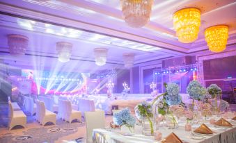 A ballroom is arranged for an event, with tables and chairs, illuminated by overhead lighting at Glory Charm Hotel
