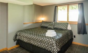 a neatly made bed with a black and white patterned comforter , pillows , and towels in a room with a window at Roxbury Suites
