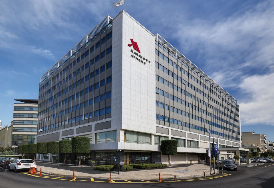 a large white building with the logo of the hyatt regency hotel in red and black letters , situated on a city street at Athens Marriott Hotel