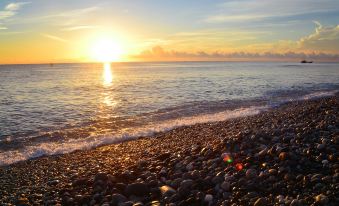 a beautiful beach scene with a sunset , pebbles , and the sun shining brightly in the sky at Ocean Hotel