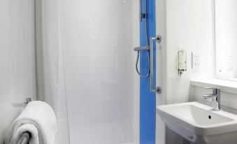 a bathroom with a blue shower head , white toilet , and sink , as well as a towel hanging on the side at Travelodge St. Clears Carmarthen