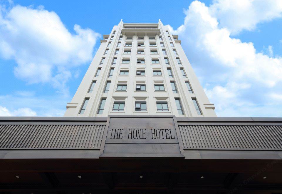 "a tall white building with the name "" the home hotel "" on top , under a clear blue sky with clouds" at The Home Hotel