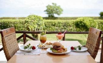 a table is set with plates of food and drinks , including a burger , fries , and a cocktail at Mitsis Galini