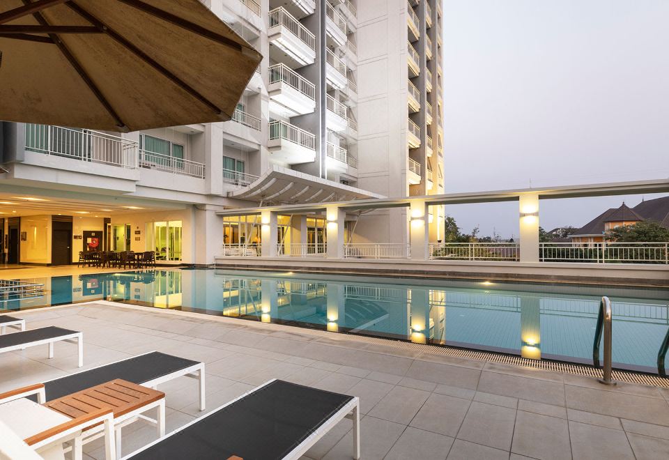 a large swimming pool is surrounded by white lounge chairs and a tall building with balconies at Kantary Hotel Kabinburi