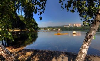 a serene lake with a paddle boat floating on the water , surrounded by trees and buildings at Hotel 99