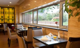 A restaurant with large windows and tables in the center, flanked by two rows at Merchant Marco Edgelake Hotel