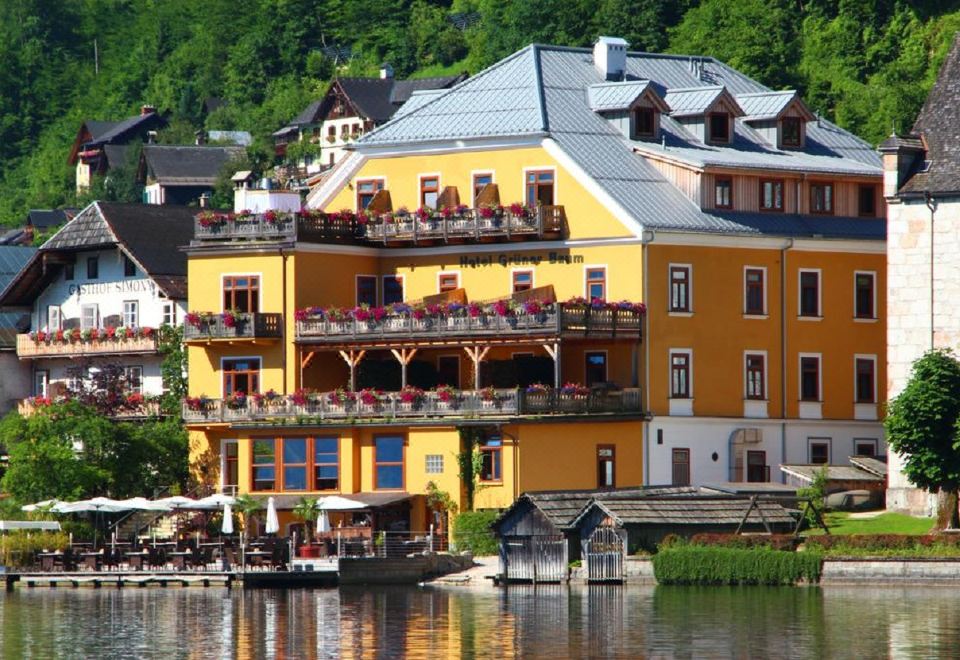 a large yellow building with balconies and restaurants is situated on the shore of a lake at Seehotel Grüner Baum