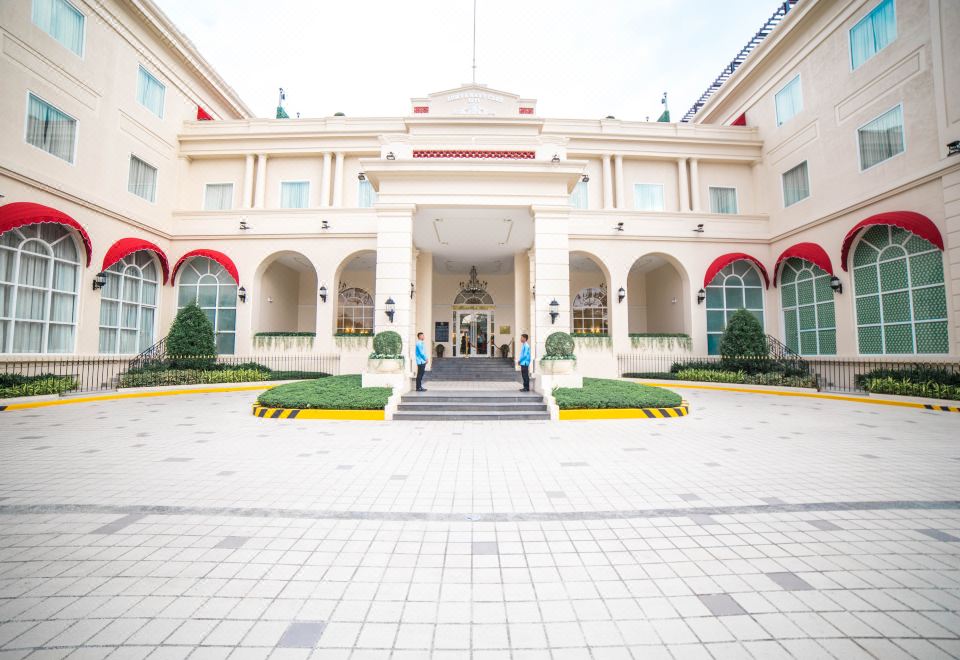a grand white building with a red trim , surrounded by greenery and a large courtyard at Rizal Park Hotel
