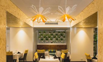 a restaurant with a dining area featuring white tables and chairs , yellow lights hanging from the ceiling , and a green wall at Metro Hotel Perth