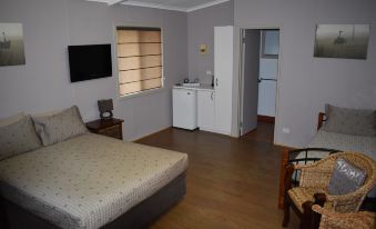 a bedroom with a bed , a chair , and a kitchenette in the background , all decorated in gray and white at Parry Creek Farm Tourist Resort & Caravan Park