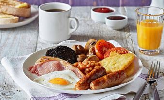 a plate of breakfast food , including eggs , sausage , bacon , mushrooms , tomatoes , and hash browns , is placed on a wooden table next at Premier Inn Sheffield City Centre (St Mary's Gate)