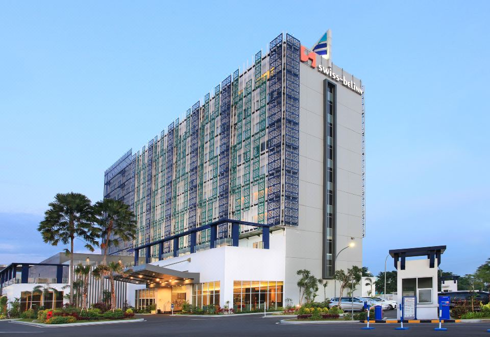 a tall building with a flag on top is surrounded by trees and a parking lot at Swiss-Belinn Modern Cikande