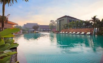 a large outdoor swimming pool surrounded by lush greenery , with several lounge chairs placed around the pool area at Mida Resort Kanchanaburi