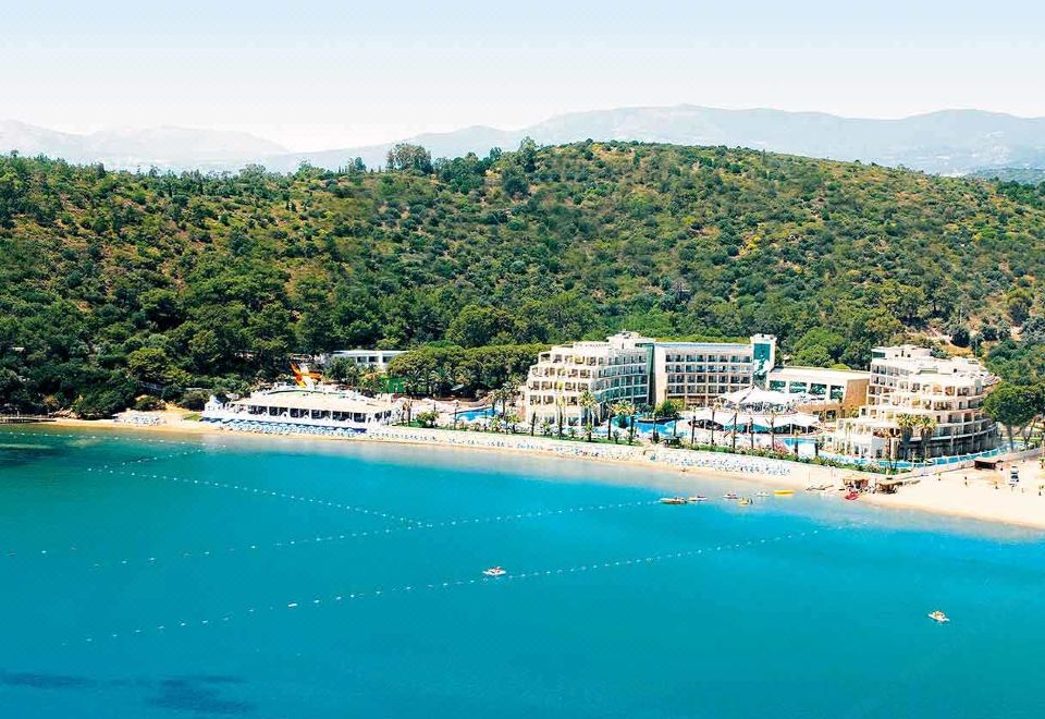 a beautiful beach scene with a hotel situated on the shore , surrounded by lush greenery at Paloma Pasha