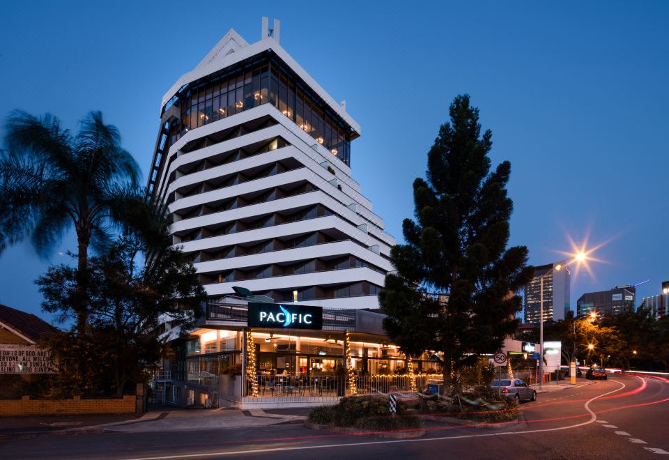 a tall hotel building with a restaurant on the ground floor , surrounded by trees and other buildings at Mercure Brisbane Spring Hill