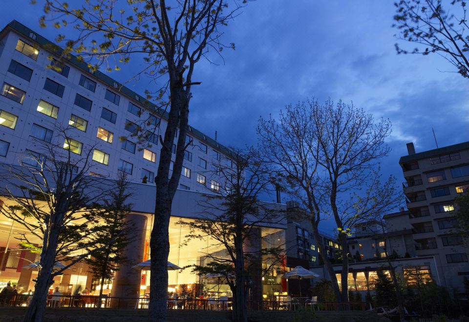 a nighttime scene of a tall building surrounded by trees , with a city skyline visible in the background at Lake Akan Tsuruga Wings