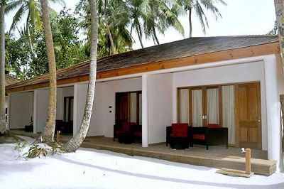 a white building with red shutters and a brown roof is surrounded by palm trees at Vilamendhoo Island Resort & Spa