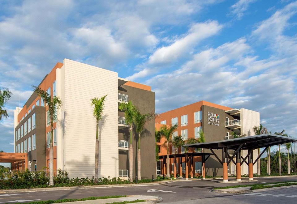 a large , modern apartment building with palm trees in the background and a parking lot in front at Four Points by Sheraton Puntacana Village