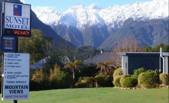 a view of a mountainous landscape with a house and sign in the foreground , and a green lawn and trees in the background at Sunset Motel