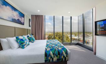 a large bed with colorful bedding is in a room with a window overlooking the city at Mantra Albury Hotel