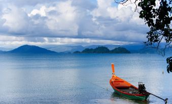 a boat is floating on a lake with mountains in the background and clouds in the sky at Phayamas Private Beach Resort and Island Brew - Adults Only