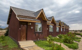 a row of small , brown houses with wooden roofs and doors , situated in a grassy area at AA Lodge Amboseli
