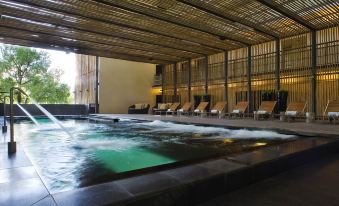 a large indoor pool with a waterfall feature and lounge chairs on the side , under a wooden roof at Hotel Maya Kuala Lumpur City Centre