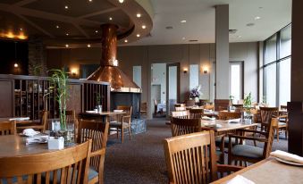 a dining room with wooden chairs and tables , a large oven on the wall , and windows at The Explorer Hotel