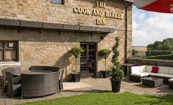 "a stone building with the sign "" the cook and barker inn "" on it , surrounded by green grass and outdoor furniture" at The Cook and Barker Inn
