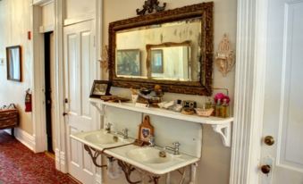 a bathroom with a large mirror , two sinks , and various toiletries on the counter , giving it an elegant and cozy atmosphere at Grand Victorian Inn