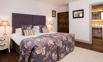 a large bed with a floral patterned comforter is in a room with white walls and wooden doors at The Lamb at Angmering