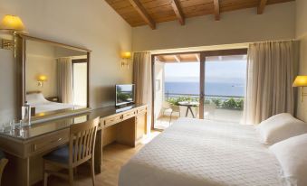 a spacious bedroom with a large bed , a desk , and a window overlooking the ocean at Negroponte Resort Eretria