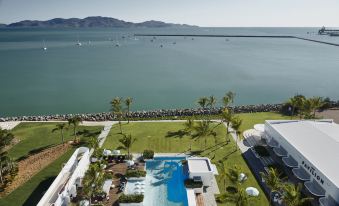 aerial view of a resort with a large pool surrounded by palm trees and a body of water in the background at The Ville Resort - Casino