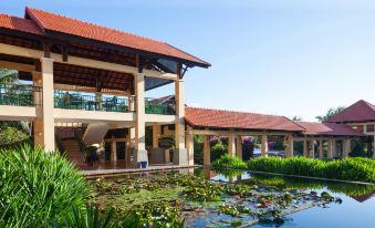 a large building with a red roof is situated next to a pond with lily pads at Pandanus Resort