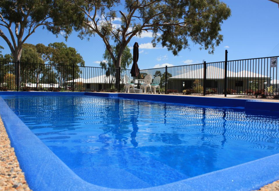 a blue swimming pool surrounded by a black fence , with trees and buildings visible in the background at Casa Nostra Motel