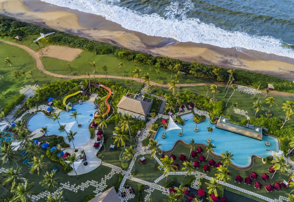 aerial view of a large resort with multiple swimming pools , palm trees , and a beach in the background at Shangri-La's Hambantota Golf Resort and Spa, Sri Lanka