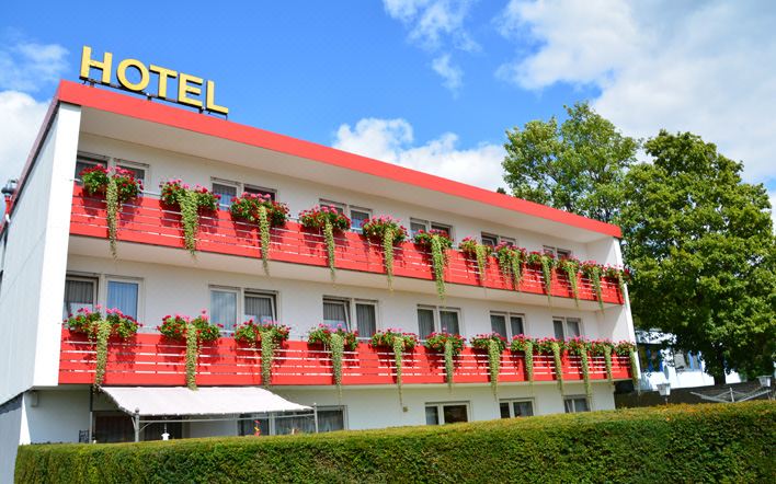 a red and white hotel with many balconies , surrounded by green grass and trees , under a blue sky with clouds at Hoffmann