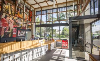 a large room with a high ceiling and glass windows , featuring a wooden counter and a woman standing near the window at YHA Byron Bay