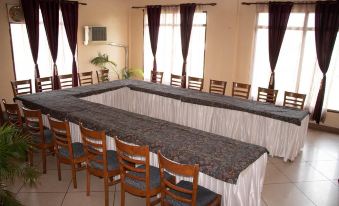 a long dining table with white tablecloth and chairs is set up in a room with large windows at Hotel Grand Riviera