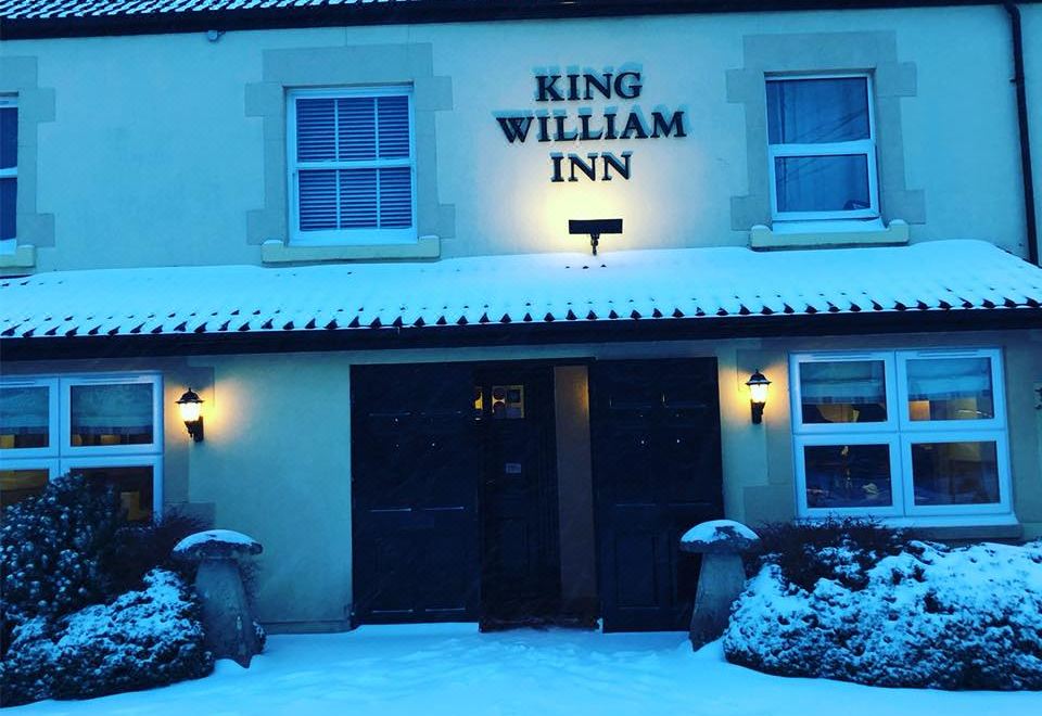 "a snow - covered building with the name "" king william inn "" written on it , surrounded by trees and bushes" at King William Inn