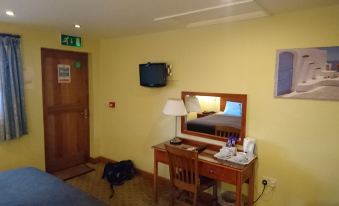 a hotel room with a television mounted on the wall , a desk with a lamp , and a chair at The Corners Inn