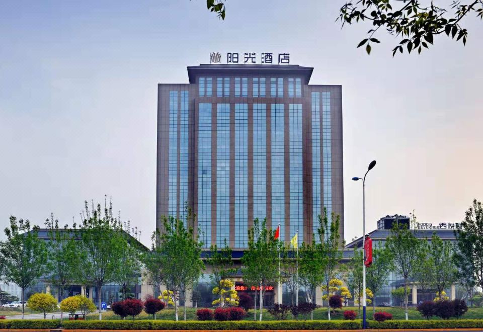 a tall building with a sign on top and trees in front of it , set against a blue sky at Sunshine Hotel