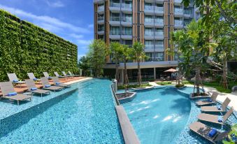 an outdoor swimming pool surrounded by a building , with lounge chairs and umbrellas placed around the pool at Hotel Amber Pattaya