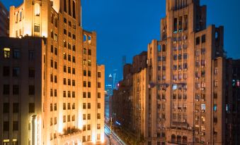 At night, a cityscape is illuminated by the lights from various buildings, including one prominent structure at Metropolo Xin Cheng Hotel, The Bund Shanghai