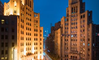 At night, a cityscape is illuminated by the lights from various buildings, including one prominent structure at Jinjiang Metropolo Hotel Classiq, Shanghai Bund Circle