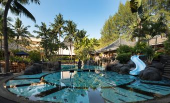 a man swimming in a large outdoor pool , surrounded by lush greenery and palm trees at Meliá Purosani